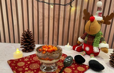 Fotografia em tons de vermelho e natal com uma taça de vidro e pavê de chocolate e morango ao centro.