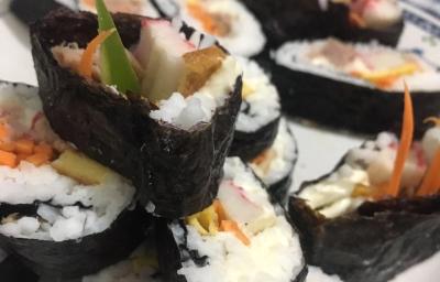 Fotografia de fatias grossas de gimbap brasileiro com arroz, cenoura, kani e pepino sobre um prato branco.