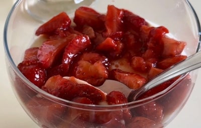 Fotografia de dois recipientes pequenos de vidro fundos sobre uma mesa branca. Dentro dos recipientes têm uma a receita de Panna Cotta com Morango e Vinagre Balsâmico.
