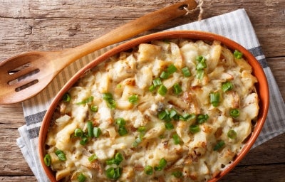 Em cima de uma mesa, recipiente com bacalhau e queijo gratinado, decorado com cebolinha picada.