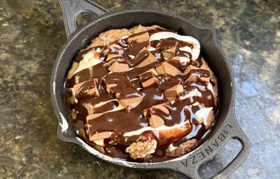 Foto vista de cima da receita de S'Mores de KitKat, preparada e servida em uma pequena panela de ferro, decorada com muita calda de chocolate e pedaços de KitKat