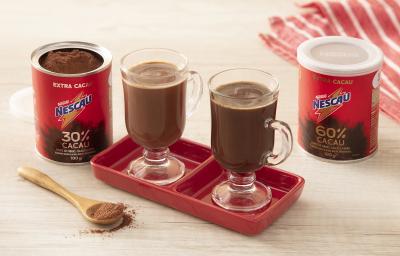 Receita do cappuccino thermogenico feita com NESCAU Extra Cacau servida em duas xícaras de vidro sobre um suporte de porcelana vermelho. Esses elementos sobre uma mesa de madeira com duas latas de nescau, um pano listrado e uma colher de nescau decorando. Receita do cappuccino thermogenico feita com NESCAU Extra Cacau servida em duas xícaras de vidro sobre um suporte de porcelana vermelho. Esses elementos sobre uma mesa de madeira com duas latas de nescau, um pano listrado e uma colher de nescau decorando.