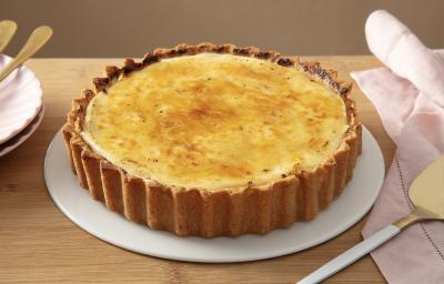 Foto da receit ade torta de limão brulée servida em uma porção grande sobre um prato branco em cima de uma mesa de madeira com um paninho rosa ao lado