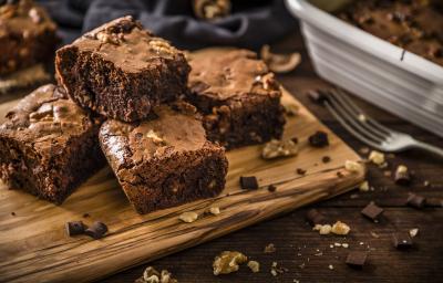 Fotografia de quatro pedaços de brownie feito de farinha de soja, castanha e chocolate. Os pedaços estão sobre uma tábua de madeira perto de um garfo. Fotografia de quatro pedaços de brownie feito de farinha de soja, castanha e chocolate. Os pedaços estão sobre uma tábua de madeira perto de um garfo.