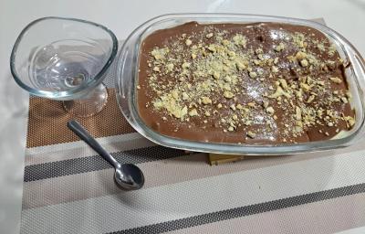 Foto da receita de Pavê de Cupuaçu com Ganache de Chocolate. Observa-se uma travessa retangular com o doce decorado de biscoito picado por cima e ao lado esquerdo tem uma taça individual. Foto da receita de Pavê de Cupuaçu com Ganache de Chocolate. Observa-se uma travessa retangular com o doce decorado de biscoito picado por cima e ao lado esquerdo tem uma taça individual.