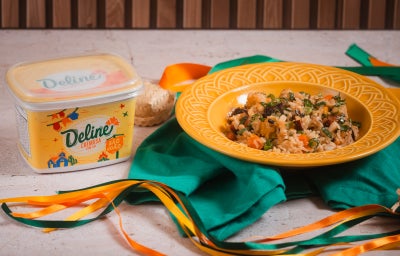 Baião de Dois junino cremoso com carne seca, bacon e calabresa servido em prato amarelo ao lado de Margarina Deline