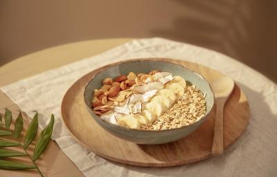 Foto em tons de bege da receita de bowl de manga com aveia servida em um bowl de cerâmica irregular sobre uma tábua circular de madeira com uma colher de madeira ao lado. Tudo sobre uma mesa com uma toalinha bege mais clara por cima