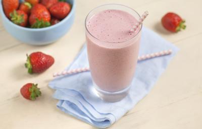 Fotografia em tons de rosa e azul de uma bancada rosa com um paninho azul, sobre ele um copo de vitamina com um canudo. Ao lado morangos. Ao fundo um recipiente redondo azul com morangos. Fotografia em tons de rosa e azul de uma bancada rosa com um paninho azul, sobre ele um copo de vitamina com um canudo. Ao lado morangos. Ao fundo um recipiente redondo azul com morangos.