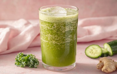Imagem mostra um copo transparente com uma bebida verde dentro, folhas de couve decoram