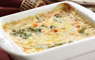 Fotografia em tons de vinho em uma bancada com uma toalha vinho, um recipiente branco retangular com os legumes gratinados dentro dele.