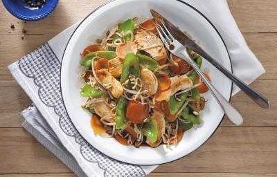 Fotografia em tons de marrom com um pano branco com detalhes azuis, um prato branco redondo raso com o frango oriental com legumes.