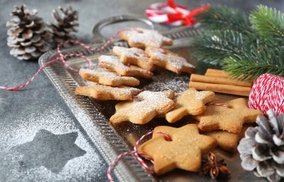 Em cima de uma mesa decorada com enfeites de natal, prato com biscoitos dourados e crocantes em formato de estrela, decorados com açúcar refinado.