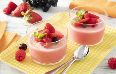 Foto da receita de Gelatina Cremosa. Observa-se dois potes de vidro com a gelatina vermelha dentro e morangos e mirtilos decorando o topo. Foto da receita de Gelatina Cremosa. Observa-se dois potes de vidro com a gelatina vermelha dentro e morangos e mirtilos decorando o topo.