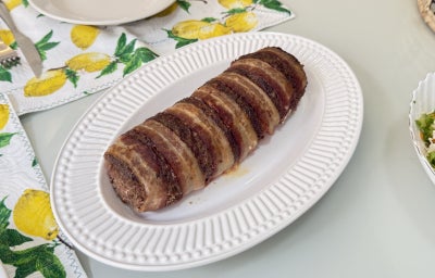 Foto vista de cima da receita de rocambole de carne com aveia, servido em um prato oval branco, bem dourado e assado, numa mesa de almoço
