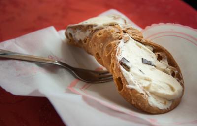 Fotografia de um cannoli de chocolate com creme branco sobre um papel, e ao lado de um garfo.