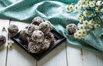 fotografia em tons de marrom, cinza e azul de uma bancada cinza vista de frente. Contém um prato quadrado preto com as balas de chocolate cobertas por coco ralado, e ao lado um pano azul com flores brancas. fotografia em tons de marrom, cinza e azul de uma bancada cinza vista de frente. Contém um prato quadrado preto com as balas de chocolate cobertas por coco ralado, e ao lado um pano azul com flores brancas.