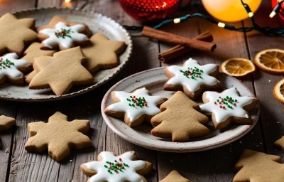 Em cima de uma mesa, prato redondo com biscoitos em forma e estrelas e árvore de Natal, decorados com glacê branco e confeitos de bolinhas coloridas. Em cima de uma mesa, prato redondo com biscoitos em forma e estrelas e árvore de Natal, decorados com glacê branco e confeitos de bolinhas coloridas.