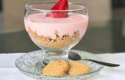Fotografia mostra uma taça transparente mostrando camadas de biscoito triturado e iogurte de morango.