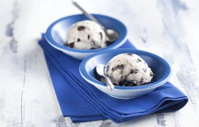 Fotografia em tons de azul em uma bancada de madeira clara, um pano azul, dois potinhos azuis redondos com o sorvete feito com Biscoito Negresco. Fotografia em tons de azul em uma bancada de madeira clara, um pano azul, dois potinhos azuis redondos com o sorvete feito com Biscoito Negresco.