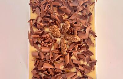 Fotografia mostra um pavê com raspas de chocolate branco e biscoito champanhe de chocolate ao centro.