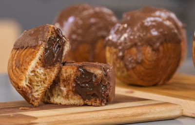Imagem da receita de New York Rolls, servida sobre uma tábua de madeira, a da frente cortada ao meio mostrando o chocolate derretendo dentro e outros dois no fundo inteiros