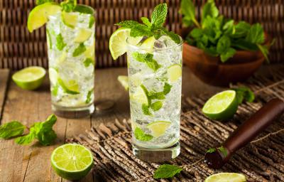Foto da receita de Mojito Sem Álcool. Observa-se dois copos altos cheio de gelo e hortelã com a bebida dentro, decorado de limões.
