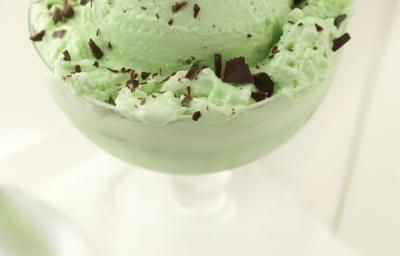 Fotografia de uma bola de sorvete de menta com chocolate em uma taça, que está sobre uma mesa branca. E, ao lado da taça, uma colher de sobremesa. Fotografia de uma bola de sorvete de menta com chocolate em uma taça, que está sobre uma mesa branca. E, ao lado da taça, uma colher de sobremesa.