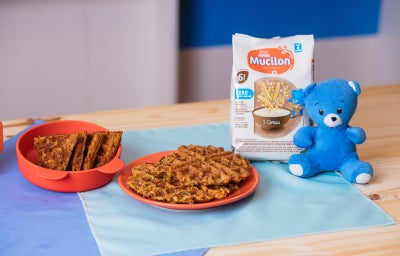 Fotografia em tons de azul em uma bancada de madeira e panos azuis, com um prato laranja e waffle em cima.