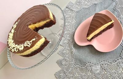 Foto da receita de torta bownie de maracujá, servida em um prato transparente, ao lado de um prato rosa em formato de coração, em uma mesa com uma toalha cinza