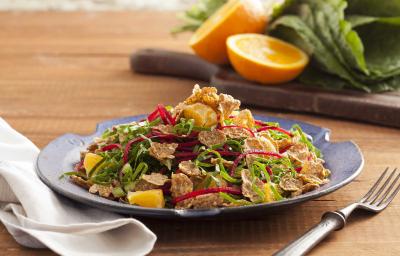 Fotografia em tons de verde em uma bancada de madeira com um prato azul ao centro com a salada de couve fininha. Ao fundo, uma tábua de madeira com couve e uma laranja cortada ao meio. Fotografia em tons de verde em uma bancada de madeira com um prato azul ao centro com a salada de couve fininha. Ao fundo, uma tábua de madeira com couve e uma laranja cortada ao meio.