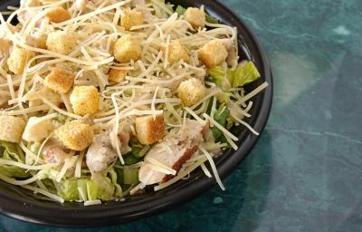fotografia em tons de azul, preto, amarelo e verde de uma bancada azul vista de cima. Contém um recipiente redondo preto com a salada, e pedaços de frango e queijo ralado. fotografia em tons de azul, preto, amarelo e verde de uma bancada azul vista de cima. Contém um recipiente redondo preto com a salada, e pedaços de frango e queijo ralado.
