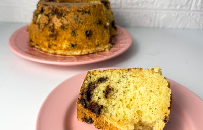 Fotografia em tons claros com um bolo de massa clara com pedaços de chocolate ao leite.