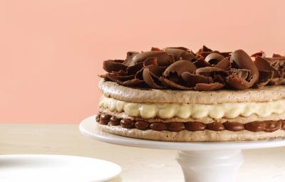 Fotografia em tons de rosa em uma mesa de madeira branca com um pano de prato vermelho, uma parede de fundo rosa, um suporte para bolo branco com a torta de macaron de chocolate e creme de avelã. Fotografia em tons de rosa em uma mesa de madeira branca com um pano de prato vermelho, uma parede de fundo rosa, um suporte para bolo branco com a torta de macaron de chocolate e creme de avelã.