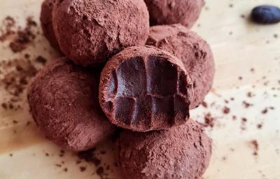 Fotografia de várias trufas de cacau e café passadas no cacau em pó. A trufa da frente foi mordida, e as trufas estão sobre uma tábua de madeira clara. Fotografia de várias trufas de cacau e café passadas no cacau em pó. A trufa da frente foi mordida, e as trufas estão sobre uma tábua de madeira clara.