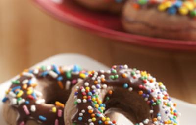 Fotografia em tons de marrom, branco e vermelho de uma bancada de madeira, sobre ela um prato branco com um donuts. Ao fundo um prato vermelho com donuts. Fotografia em tons de marrom, branco e vermelho de uma bancada de madeira, sobre ela um prato branco com um donuts. Ao fundo um prato vermelho com donuts.