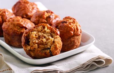 Fotografia de alguns muffins de maçã sobre um apoio retangular branco, o qual está apoiado em um paninho também branco. O pano está sobre uma bancada de cimento queimado claro. Fotografia de alguns muffins de maçã sobre um apoio retangular branco, o qual está apoiado em um paninho também branco. O pano está sobre uma bancada de cimento queimado claro.
