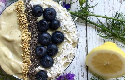 Fotografia em tons de roxo em uma bancada de madeira com um bowl e o creme de avocado dentro dele, decorado com mirtilo, castanha-de-caju e sementes de chia. Ao lado, limão siciliano na mesa. Fotografia em tons de roxo em uma bancada de madeira com um bowl e o creme de avocado dentro dele, decorado com mirtilo, castanha-de-caju e sementes de chia. Ao lado, limão siciliano na mesa.