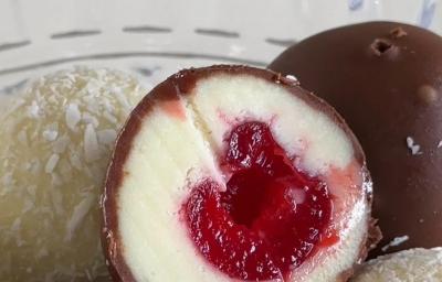 Fotografia em tons claros de um bombom de cereja com casquinha de chocolate, tem outro passados apenas no coco ralado.
