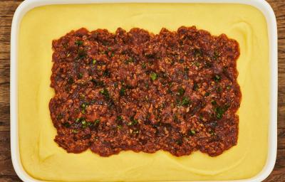 Foto bem aproximada de uma travessa branca. Dentro dela está a receita de polenta em tom amarelo claro e, ao centro, a carne moída com molho Foto bem aproximada de uma travessa branca. Dentro dela está a receita de polenta em tom amarelo claro e, ao centro, a carne moída com molho