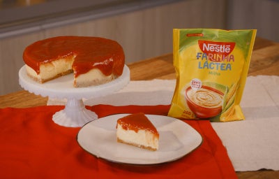 imagem mostra uma cheesecake cremosa de milho com cobertura de goiabada em uma forma redonda.