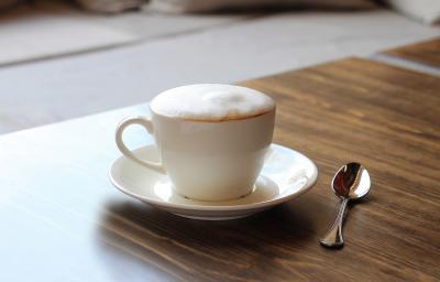 fotografia em tons de marrom e branco tirada de uma bancada marrom. Contém um pratinho branco com uma xicara de café branca, e dentro contém a bebida Cappuccino. fotografia em tons de marrom e branco tirada de uma bancada marrom. Contém um pratinho branco com uma xicara de café branca, e dentro contém a bebida Cappuccino.