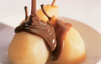 Fotografia em tons de amarelo em uma bancada de madeira branca, um prato redondo raso branco com as peras e calda de chocolate em cima dele. Fotografia em tons de amarelo em uma bancada de madeira branca, um prato redondo raso branco com as peras e calda de chocolate em cima dele.