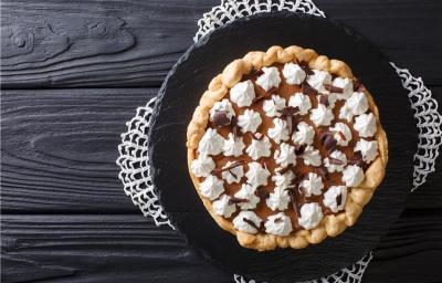 Fotografia vista de cima de uma torta redonda com chantilly em bicos com raspas de chocolate. A torta está sobre um apoio preto, o qual está apoiado em uma mesa de madeira preta. Fotografia vista de cima de uma torta redonda com chantilly em bicos com raspas de chocolate. A torta está sobre um apoio preto, o qual está apoiado em uma mesa de madeira preta.