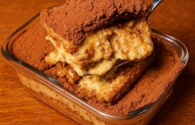 Fotografia em tons terrosos com uma travessa de vidro ao centro. Dentro da travessa existe uma receita de tiramissu feita com creme de castanha de caju, biscoito champanhe e finalizada com cacau em pó Fotografia em tons terrosos com uma travessa de vidro ao centro. Dentro da travessa existe uma receita de tiramissu feita com creme de castanha de caju, biscoito champanhe e finalizada com cacau em pó