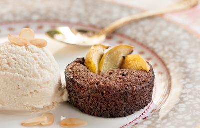 Fotografia em tons de salmão em uma bancada de madeira com uma toalha branca com detalhes salmão, um prato redondo de porcelana desenhado em cinza e rosa com uma bola de sorvete de creme e um mini bolinho de chocolate em cima dele. Fotografia em tons de salmão em uma bancada de madeira com uma toalha branca com detalhes salmão, um prato redondo de porcelana desenhado em cinza e rosa com uma bola de sorvete de creme e um mini bolinho de chocolate em cima dele.