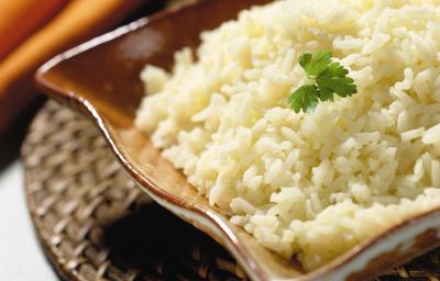 Fotografia em tons de marrom em uma mesa de madeira cinza com um descansa prato de palha marrom, um pano laranja e um recipiente retangular marrom com o arroz dentro. Fotografia em tons de marrom em uma mesa de madeira cinza com um descansa prato de palha marrom, um pano laranja e um recipiente retangular marrom com o arroz dentro.