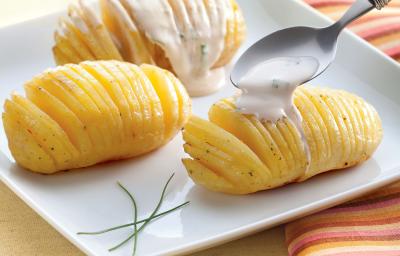 Fotografia em tons de laranja em uma bancada de madeira clara com um pano listrado em tons de laranja ao lado. Ao centro, um prato quadrado branco raso com três batatas cortadas em lâminas bem finas e temperadas com ervas finas. Fotografia em tons de laranja em uma bancada de madeira clara com um pano listrado em tons de laranja ao lado. Ao centro, um prato quadrado branco raso com três batatas cortadas em lâminas bem finas e temperadas com ervas finas.