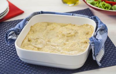 Fotografia em tons de azul e branco de uma bancada vista de cima. Contém um pano azul com um recipiente quadrado branco com alças e dentro as batatas gratinadas. Ao lado um pano azul. Fotografia em tons de azul e branco de uma bancada vista de cima. Contém um pano azul com um recipiente quadrado branco com alças e dentro as batatas gratinadas. Ao lado um pano azul.