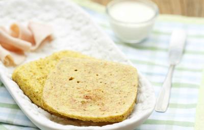 em um recipiente branco contém duas fatias de pão, abaixo dois panos nas cores verde e branco e ao lado uma xícara de leite e um garfo.