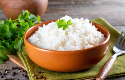 imagem mostra um recipiente com uma porção de arroz branco e folhas de salsinha verde por cima